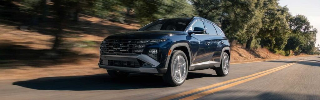 2026 Hyundai Tucson Hybrid SUV driving on a sunlit road with motion blur and trees in the background