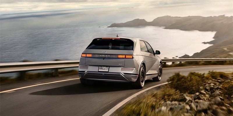 A Hyundai Ioniq-5 silver electric car driving on a coastal road with ocean and cliffs in the background