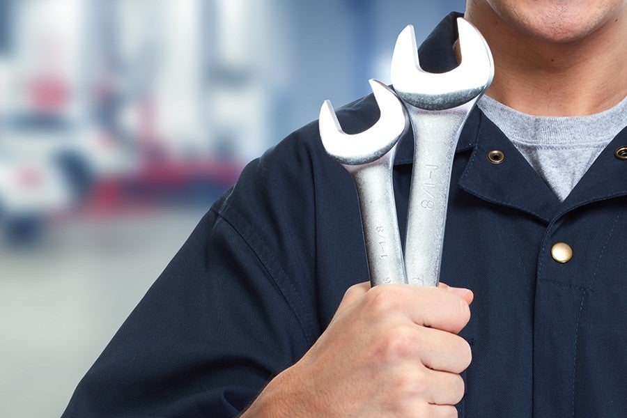Mechanic in blue uniform holding wrenches across chest