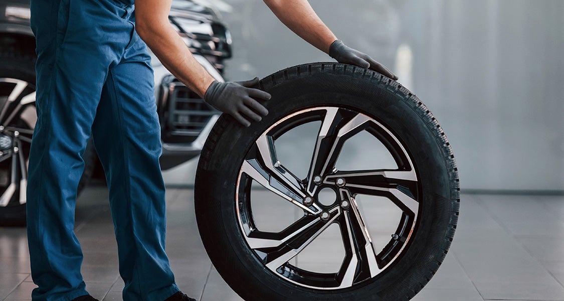 Mechanic in blue uniform holding a car tire with black gloves